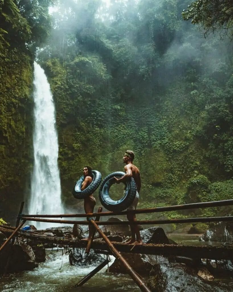 two person carrying black inflatable pool float on brown wooden bridge near waterfalls - Vacation Instagram Captions 