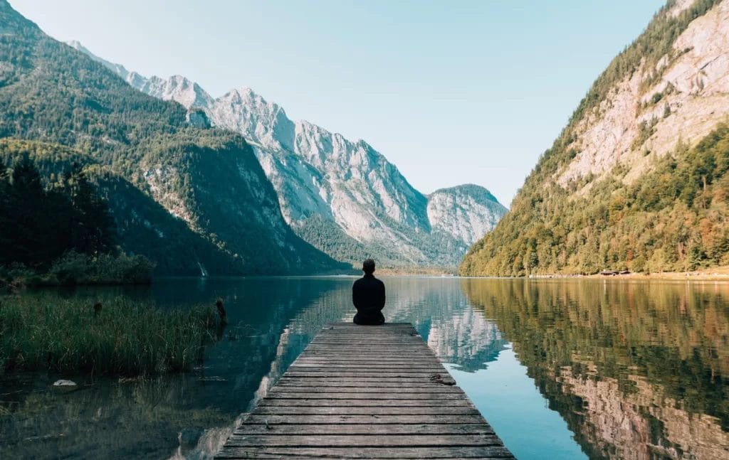 une personne assise sur des planches de bois à travers le paysage du lac