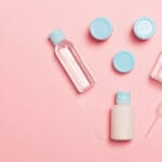 A set of travel size cosmetic products on a pink background.