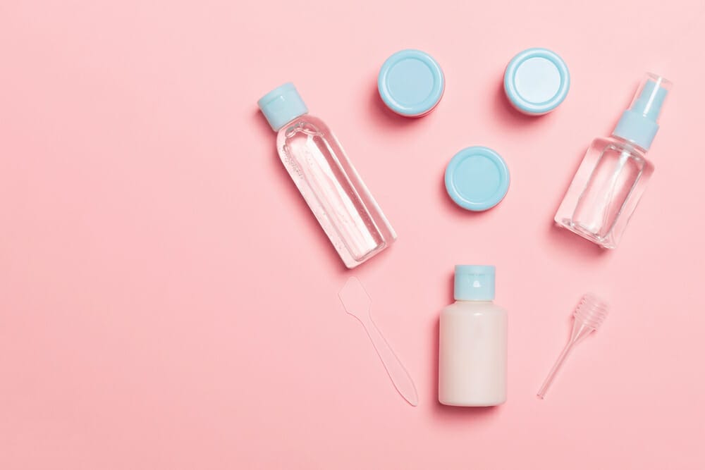 Un set di prodotti cosmetici da viaggio su sfondo rosa.