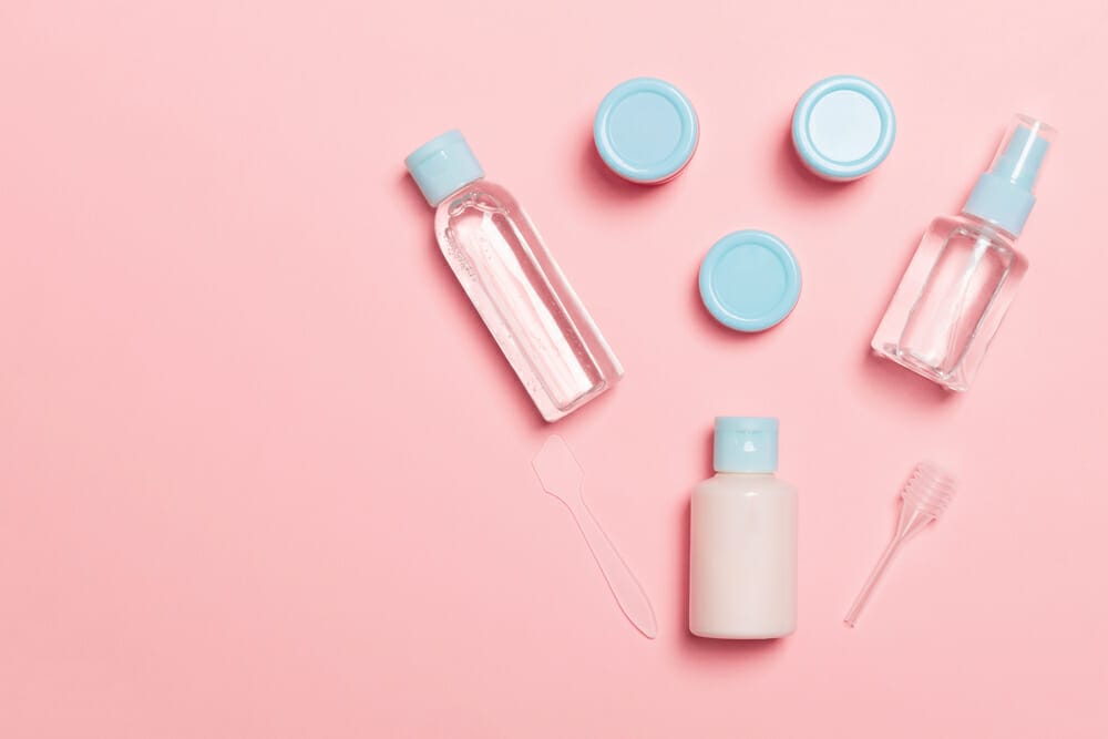 A set of travel size cosmetic products on a pink background.