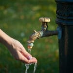 La mano di una persona versa l'acqua del rubinetto da un idrante.