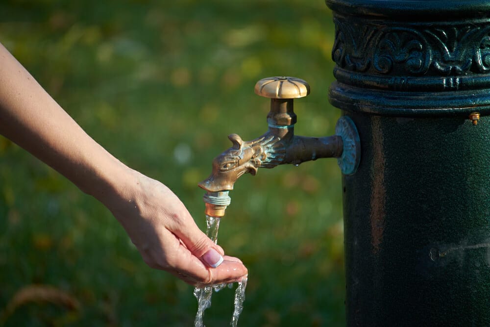 A person's hand pours tap water from a water hydrant.