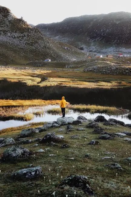 A man in a yellow jacket standing in a grassy area near a lake.