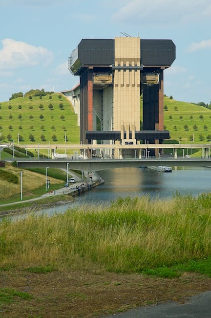 A large building sits on a grassy hill next to a body of water.