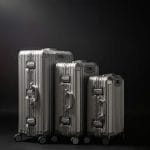 Three silver suitcases on wheels, perfect for European travel, against a black background.