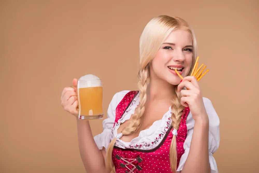 Oktoberfest Travel Guide - A woman in bavarian dress is holding a mug of beer and fries.