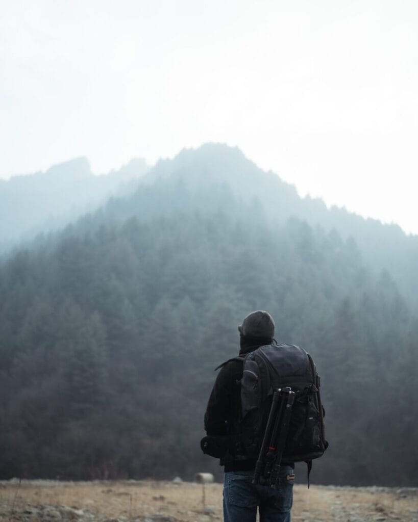 A man with a backpack standing in front of a mountain.