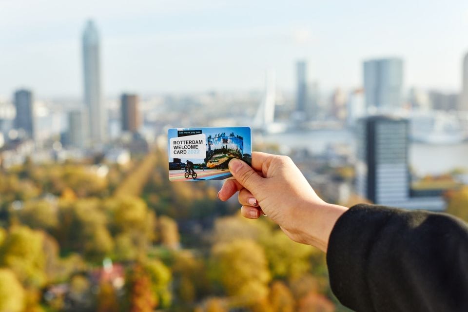 A person holding up a Rotterdam Pass card in front of a city background.