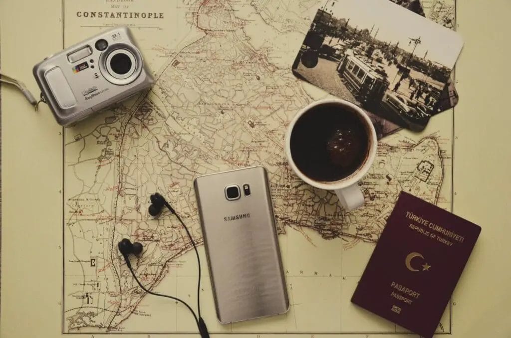 Silver Camera Near Black Coffee in Mug, Silver Samsung Galaxy S7, Turkey Passport, and Black Earbuds