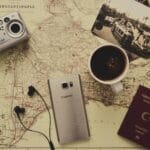 Silver Camera Near Black Coffee in Mug, Silver Samsung Galaxy S7, Turkey Passport, and Black Earbuds