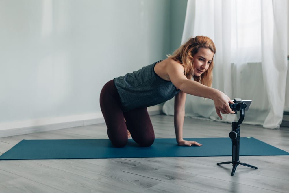 Una mujer practicando yoga sobre una colchoneta, capturada por una cámara usando uno de los mejores cardanes para teléfonos inteligentes.