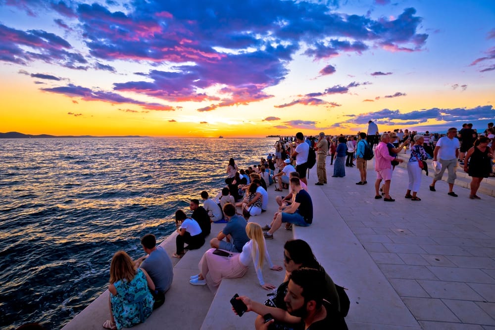 A group of people sitting on a ledge near the ocean.
