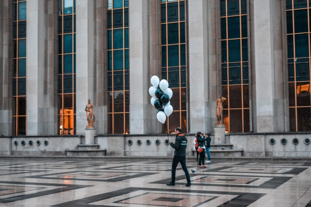 A man holding balloons in front of a building.