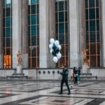 A man holding balloons in front of a building.