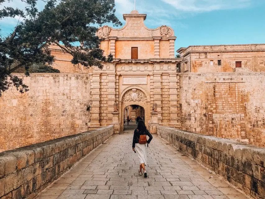 A woman exploring the Best Things to Do in Valletta, strolls down a stone path towards a castle in Malta's capital city, Valletta.