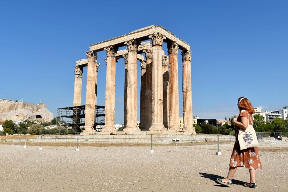 A woman is standing in front of the parthenon in athens.