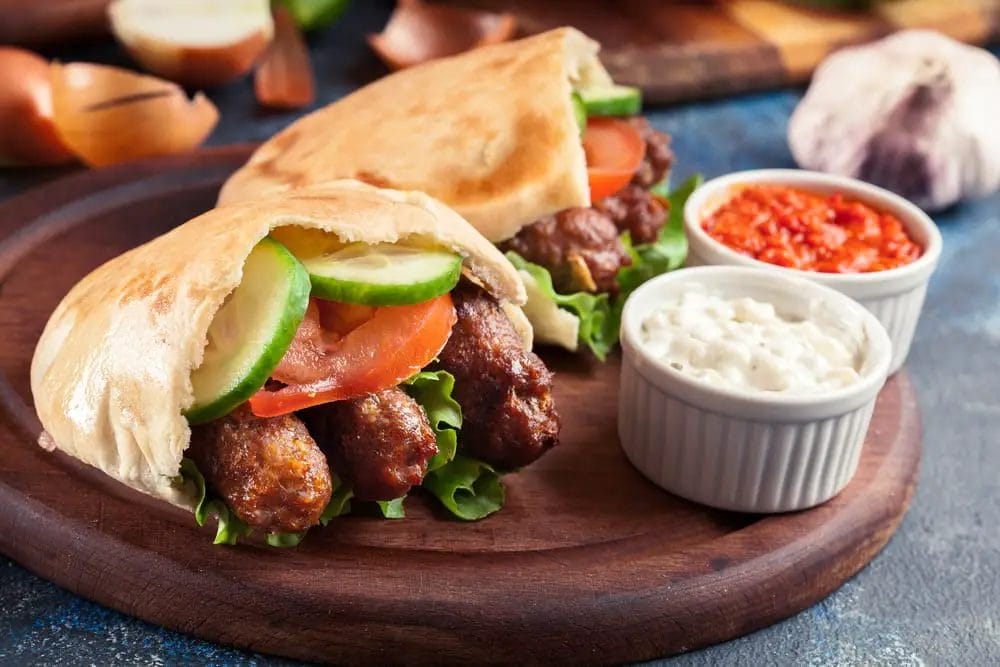 The National Dish of Bosnia, two mouthwatering pitas loaded with meat and vegetables, artfully showcased on a rustic wooden cutting board.