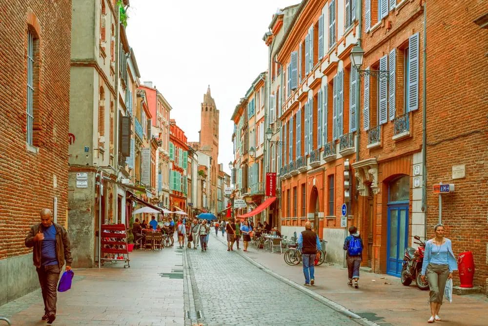 Unternehmungen im französischen Toulouse – Menschen gehen eine Kopfsteinpflasterstraße entlang.