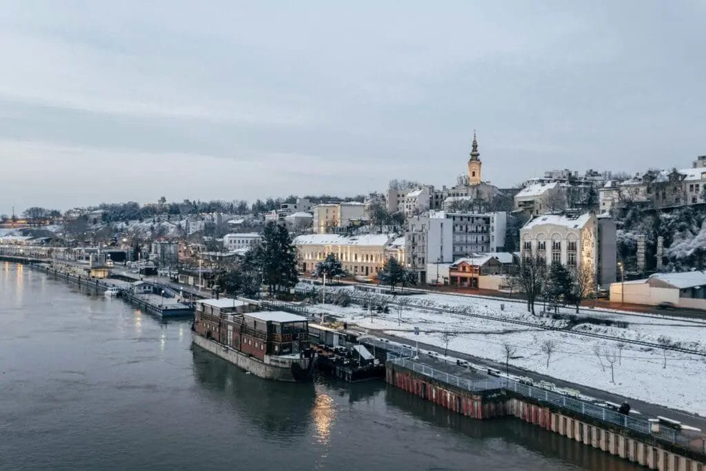 A scenic view of a frozen river and architectural structures during the winter season in Serbia.