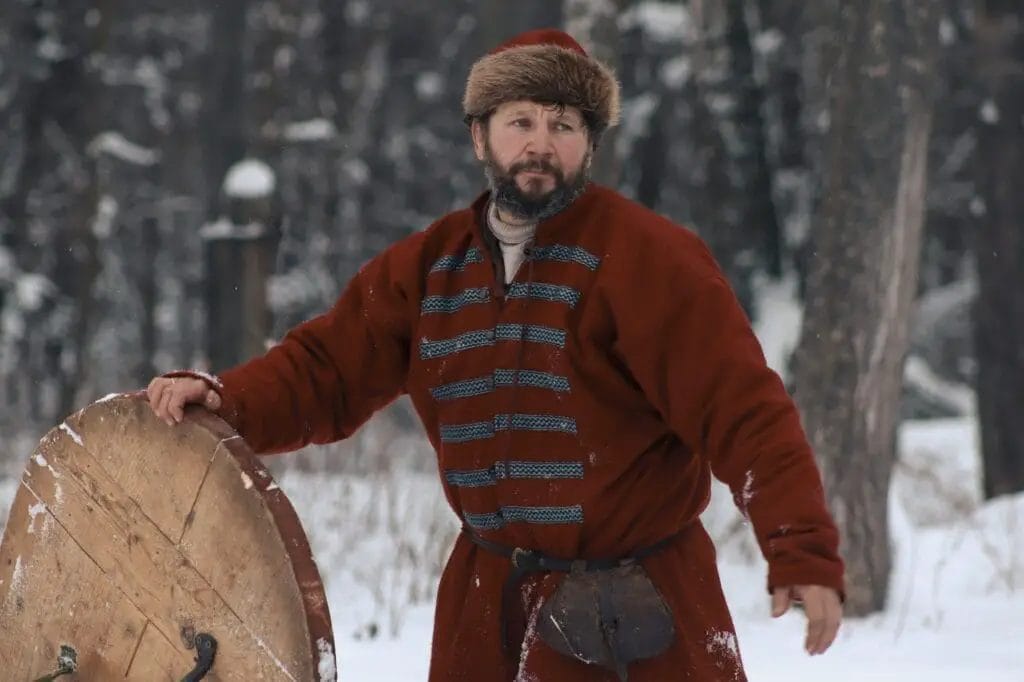 A man in a red coat is holding a wooden sled in the snow.
