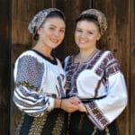 Two women in traditional clothing standing in front of a wooden wall.