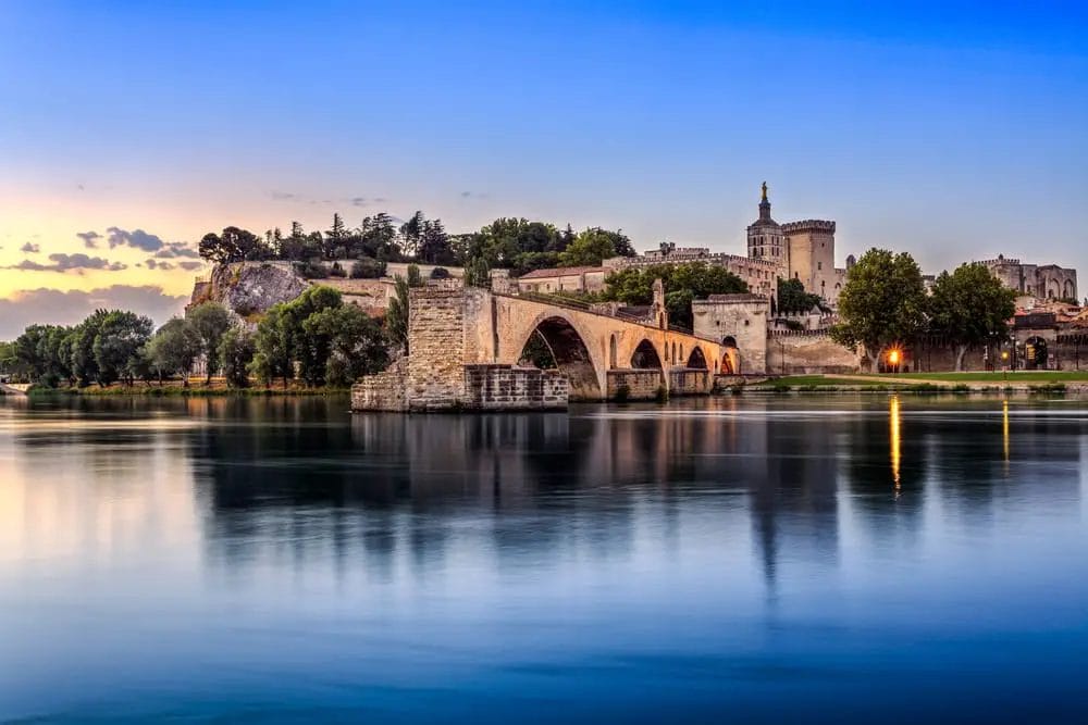 Un pittoresco castello si affaccia su un fiume mentre un incantevole ponte collega il paesaggio idilliaco, perfetto per gite di un giorno da Nizza, in Francia.