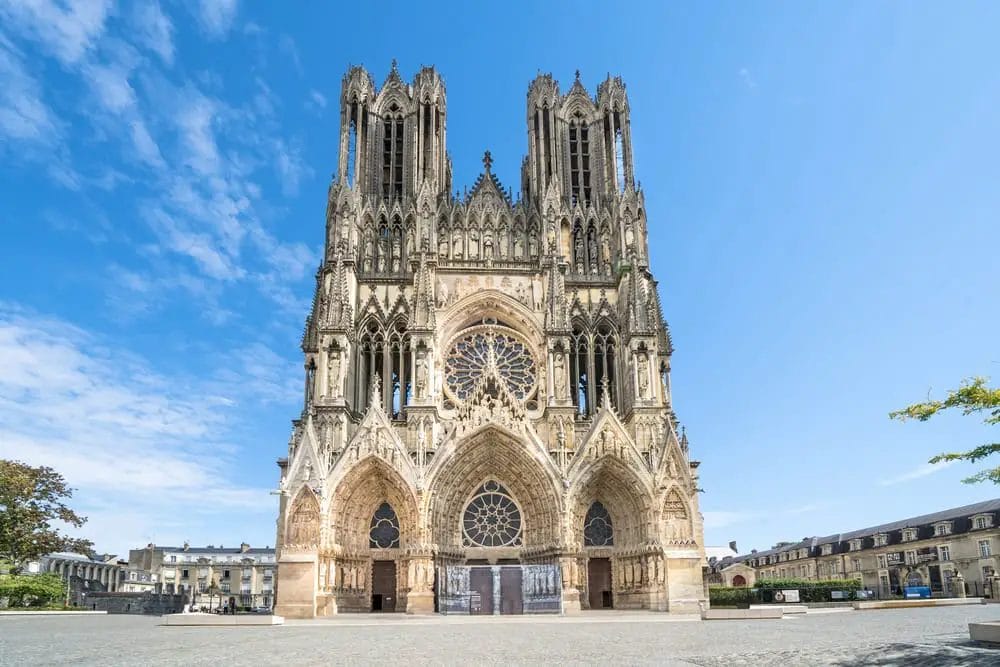 Ein großes, reich verziertes Gebäude mit einem großen Fenster und der Kathedrale von Reims im Hintergrund.