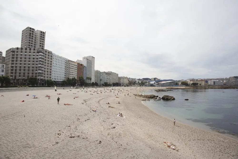 A sandy beach with a lot of people on it. 10 Best La Coruna Beaches