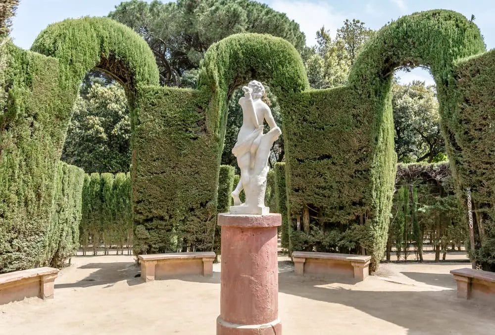 Sculpture in a Barcelona garden with manicured hedge arches.