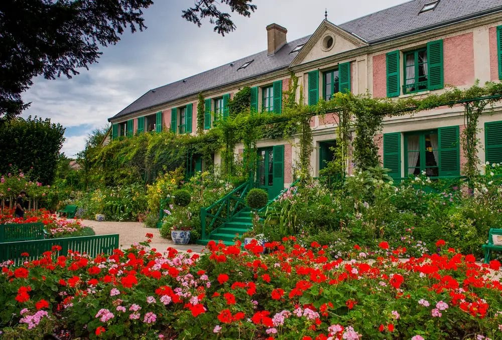 A house with red flowers and green shutters, a charming place to visit in Normandy.