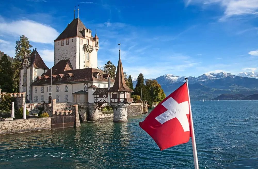 Schweizer Flagge weht vor einem malerischen Schloss am Seeufer und einer Bergkulisse in der Schweiz.