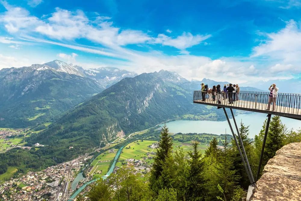 Tourists enjoying a panoramic view from a mountain lookout platform over a valley and river.