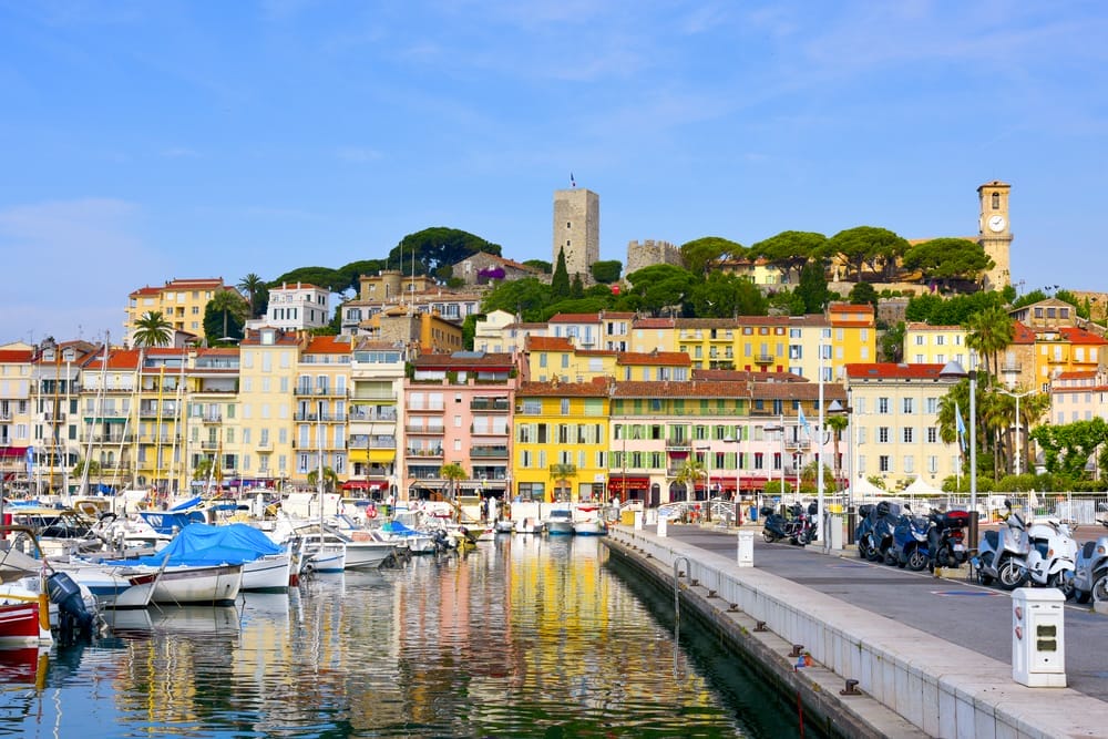 Colorful buildings and boats along a waterfront with a hilltop tower in the background.