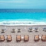 Empty beach chairs facing the sea on a pebble beach with calm blue waters in Nice.