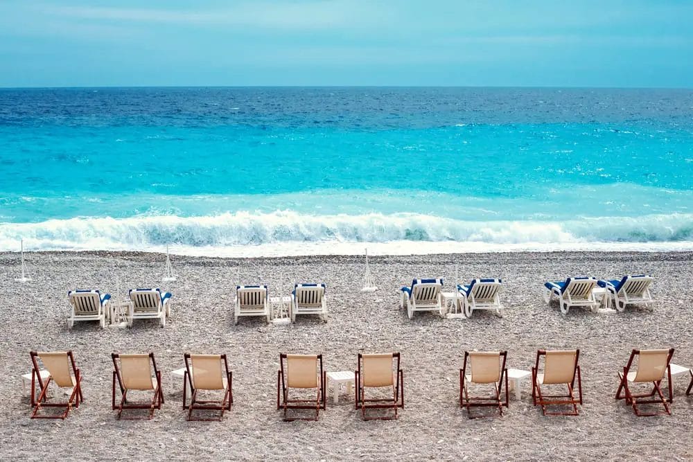 Leere Liegestühle mit Blick auf das Meer an einem Kiesstrand mit ruhigem blauen Wasser in Nizza.