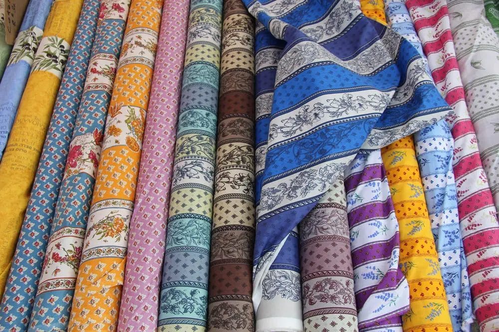 Assorted colorful fabrics rolled up on display, perfect souvenirs from shopping in Nice.