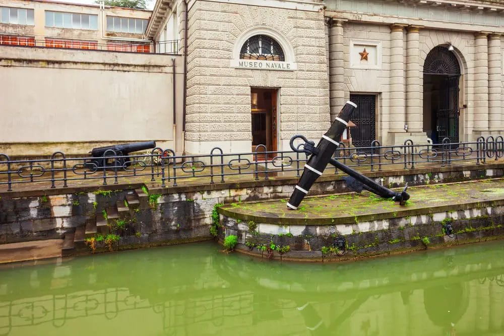 A large black and white anchor on a stone platform with green water in La Spezia.